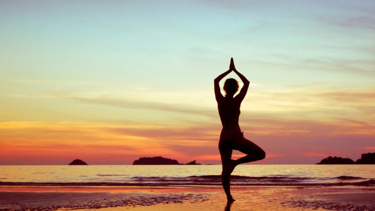 Woman practicing yoga on the beach at sunset