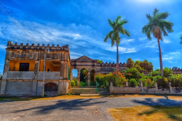 An abandoned hacienda against a blue sky and palm trees