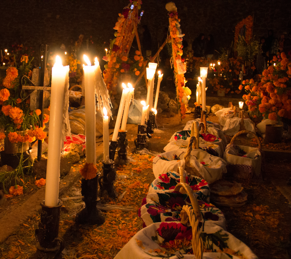 Candlelit Day of the Dead altar in a cemetery, decorated with marigolds, embroidered cloths, and offerings honouring loved ones at night.