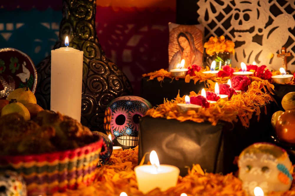 A colourful Día de Muertos altar with candles, marigold flowers, sugar skulls, food offerings, and a picture of the Virgin Mary honouring loved ones.