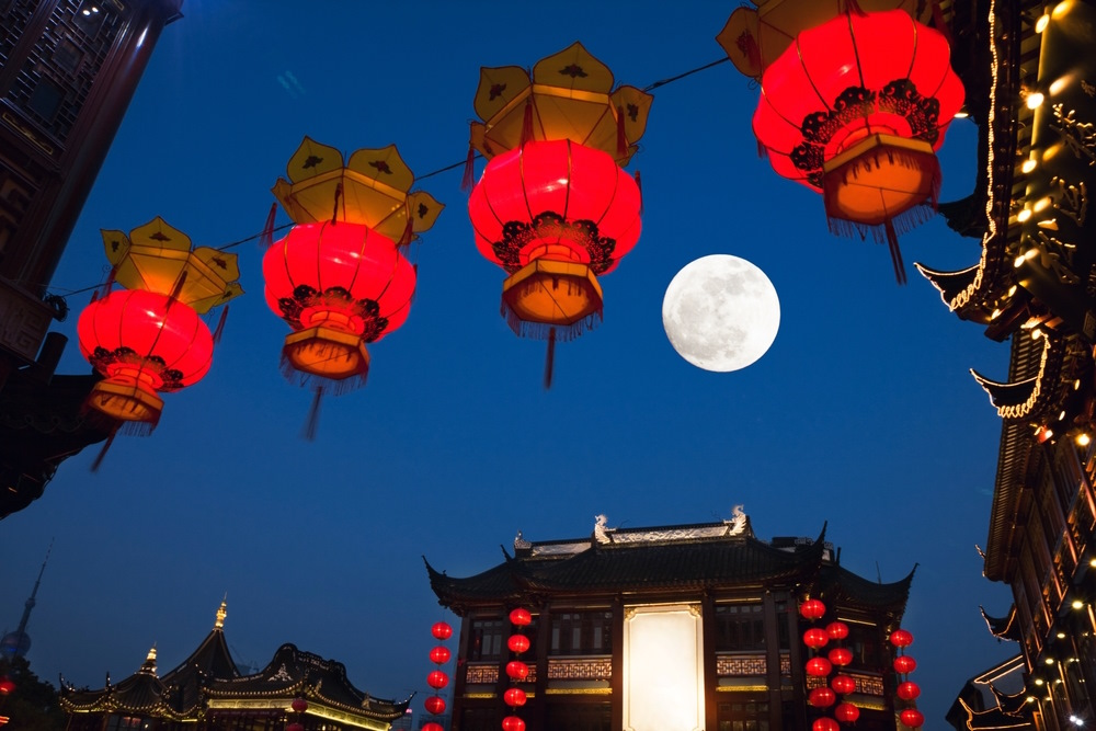 The full moon shining over red lanterns and temples roofs of the Yu Garden in Shanghai, China.